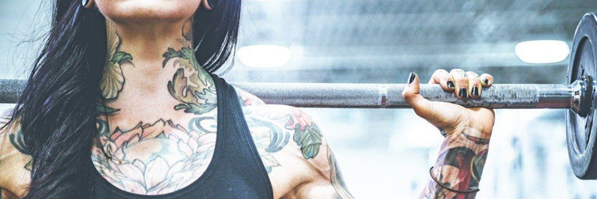 Tattooed Woman holding Bar on her Back in the Gym